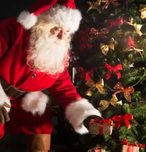 Papai Noel colocando presentes de Natal numa árvore.