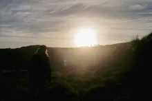 Um radiante pôr do sol sobre uma colina com uma pessoa em primeiro plano.