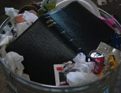 Uma Bíblia jogada sobre o lixo em uma lata de lixo.