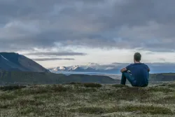 Um homem sentado no chão olhando para a paisagem.