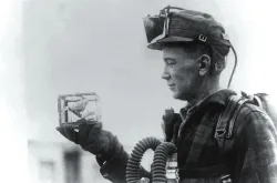 Um minerador segurando uma gaiola com um canário.