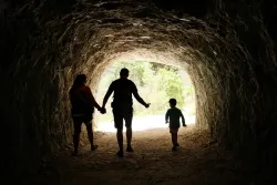 Família de três pessoas caminhando em uma caverna em direção à luz.